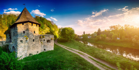 Ancient stone castle in Kamianets Podilskyi standing on hill with green trees and bushes with rural road and riverの写真素材