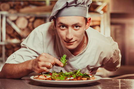 young male cook preparing delicious appetizer with herbs on white plate