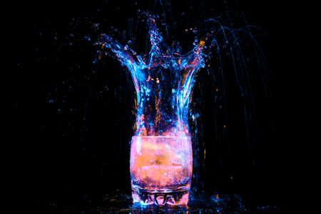 colorful cocktail in glass with splashes and lemon on dark background. Party club entertainment. Mixed lightの写真素材