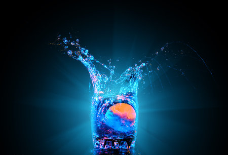 Colorful cocktail in glass with splashes and lemon on dark background. Party club entertainment. Mixed lightの写真素材