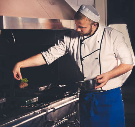 young chef preparing meat in the kitchen interiorの写真素材