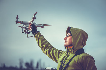 Young man in green jacket operating a drone using a remote controller.