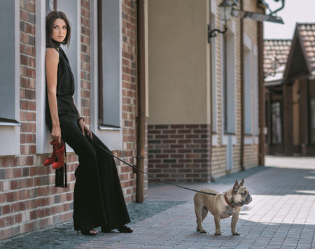 Beautiful young woman in black costume with cute small dog puppy posing on the streetの写真素材