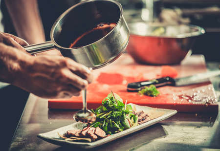 Chef finishing her plate and almost ready to serve at the table. Only hands. Finally dish dressing: steak meat with green saladの写真素材