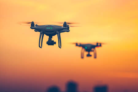 Close up photo of two Professional Remote Control Air Drones with action cameras flying in dramatic sunset sky. Modern technologies. Travel, hobby, inspiration. Pastel orange toning. Kiev, Ukraineの写真素材