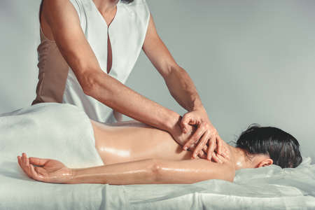 Massage oil therapy. A young professional male masseur makes Thai massage. Patient woman is lying down on a bed and is covered with white towel. Treatment, rest, relaxation, spa, health care, medicineの写真素材