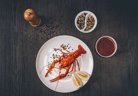 Food concept. Boiled big red fresh crawfish in white plate with lemon slices. Composition with sauce, herbs and pepper grains around. Gray wooden background. Instagram vintage toning effect. Top view.の写真素材