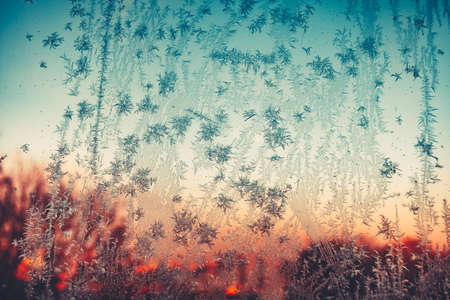 Frosty pattern. Vintage frozen ice texture on the window at sunset. Frozen snowflakes and frost over the sun on frozen Christmas winter background. Colored in blue tone. Instagram filterの写真素材