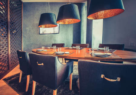Stylish inside decor of the mod restaurant. The contemporary interior the wooden round table, comfortable chairs and the modern lamps. Exquisite combination the royal blue and orange shades.の写真素材
