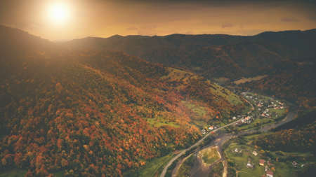 Aerial View: Beautiful canyon village located along the river. Dramatic autumn mountain landscape with green meadows, orange pine tree forests, sunset cloudy sky. Carpathians, Ukraine, Europe.の写真素材