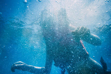 The silhouette of an attractive slim woman under water. The beauty of the ocean world. Ideal background for the different kinds of marine collages and illustrations in blue shades.の写真素材
