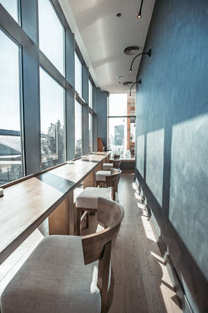 Cozy interior of the modern restaurant. Inside part of the main hall with the row of bar chairs and long bar table in front of transparent glass window. Wonderful panoramic view.の写真素材