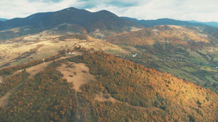 Aerial View over beautiful autumn mountain landscape. Yellow pasture with lonley houses among orange pine tree forest. Mountain range in the background. Holidays, travel. Carpathians, Ukraine, Europeの写真素材