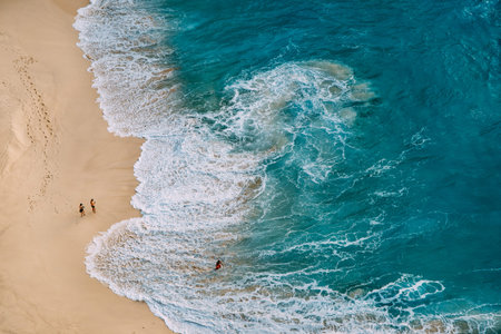 Aerial drone top view on ocean beach landscape with turquoise water, strong waves and yellow sand....
