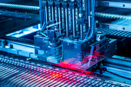 Electronic circuit under surface-mounting machine. Shot in blue toning filter. Surface-mount technology as a producing of electronic circuits. Components placed onto the surface of printed elements.の写真素材