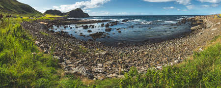 Panoramic view of Northern Ireland bay. Stunning shoreline surrounded by the boulders. Grass covered land under the blue cloudy sky. Wild nature environment. Overwhelming Irish landscape.の写真素材