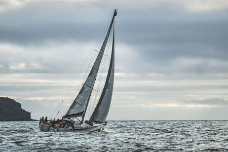 Close-up lone yacht sailing in the sea. Northern Ireland. Blue grey cloudy sky background. Outdoor tourist activity. Wild nature environment before the rain. Mysterious Irish ocean scape.の写真素材
