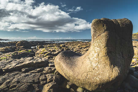 Close-up boulder on the stone beach. Cloudy rainy sky background. Northern Ireland shoreline. Sunlit smooth large rock on the stoned island surface. Horizon view. Stunning Irish landscape.の写真素材