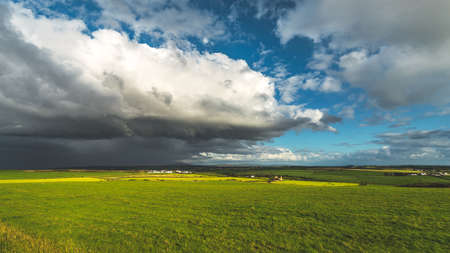Heavy rainy clouds over the Northern Ireland field. Stunning countryside landscape. Green grass covered meadow under the colorful sky before the rain. Panoramic view of the wild virgin nature.の写真素材