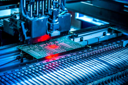 Electronic circuit under surface-mounting machine. Shot in red and blue tints. Surface-mount technology as a producing of electronic circuits. Components placed onto the surface of printed elements.の写真素材