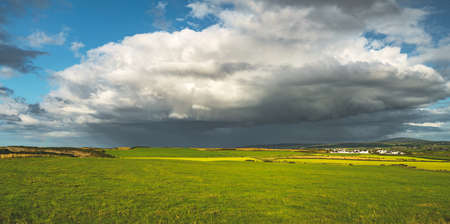 Rainy sky above the green field. Northern Ireland panoramic view. Breathtaking landscape the huge white clouds, grass covered meadow before the rain. Picturesque Irish countryside background.の写真素材