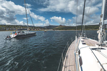 Close-up view from the yacht front sailing in the sea. Northern Ireland. Tourist boats on the water surface next to the Irish shoreline. Amazing marine scene. Outdoor activity. Cloudy sky background.の写真素材