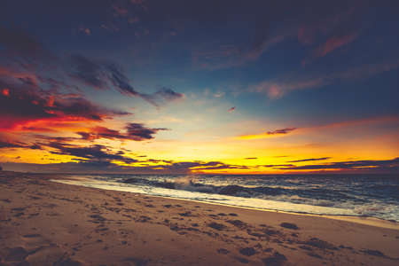 Bright sunset over the Asian shoreline. Stunning landscape. Breathtaking cloudy colorful sky over the ocean and the beach. The footprints on the sand surface. Ideal image for the backgrounds.の写真素材