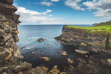 Irish bay surrounded by the green covered rocks. Northern Ireland. Amazing scene the water surface next to the Irish land. Blue cloudy sky background. Beauty of wild virgin nature. Stunning landscape.の写真素材