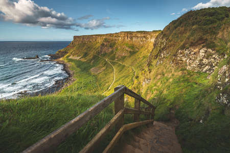 Rock stairs leading to the shore. Northern Ireland landscape. Overview of the stunning Irish shoreline. Grass covered cliffs next to the ocean. Close-up touristic trail among the wild nature.の写真素材