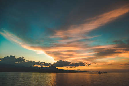 Colorful bright sunset sky over the Komodo island shore. Indonesia. Picturesque landscape. The clouds reflection on the calm water surface. The lone ship sailing into the distance. Fairy tale scene.の写真素材
