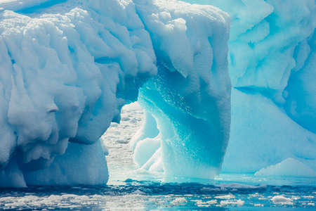Close-up arch of the iceberg. Antarctic landscape in the blue and white tints. Overwhelming scene of the ice covered glacier floating among the polar ocean. The geometric shapes of the ice mount.の写真素材
