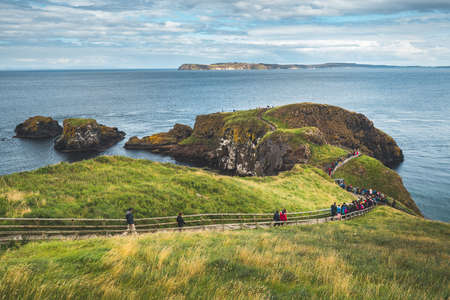 Tourists walking on the wooden path to the ocean. Northern Ireland. People hiking among the grass covered cliff to the Irish shoreline. Picturesque landscape. Ideal place for the outdoor activity.の写真素材