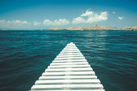 Close-up white pier leading to the ocean. Komodo island, Indonesia. Amazing marine scene. The cloudy sky over the crystal clear water. The romantic road into the distance. The conceptual image.の写真素材