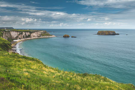Close-up Northern Ireland shoreline. Calm water surface next to the Irish cliff. Overwhelming marine scene. Irish bay under the blue cloudy sky. Perfect place for the rest and relax.の写真素材