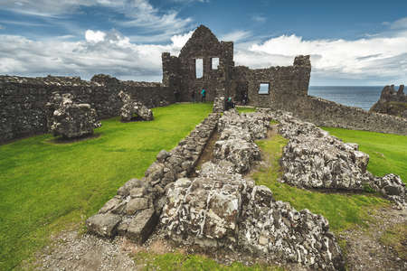 Close-up Dunluce castle ruins. Northern Ireland landscape. The tourists walking on the archeological site. The now-ruined Medieval castle with stunning ocean view. Picturesque Irish landscape.の写真素材