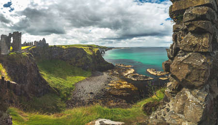 The overview from Dunluce castle to the Irish bay. Overwhelming Northern Ireland landscape. Epic shoreline view from above the cliff. The ruins of the Medieval building under the cloudy rainy sky.の写真素材