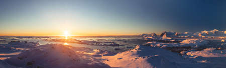 Bright colorful sunset panorama view in Antarctica Ocean. Orange sun lights over the snow covered polar surface. Picturesque winter landscape. The beauty of the wild untouched Antarctic nature.の写真素材