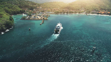 Aerial View: Ferry sailing in harbor. Travel Vacation Recreation Paradise Tourism. Sunset mountain hills in background. Beautiful nature landscape in Tropical Bali Island. Cinematic filterの写真素材