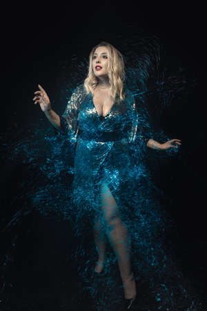 Woman blonde surrounded mix blue lights effect. Full length photo. Black background. Beautiful young woman with long hair in evening dress. Surprise expression. Fairy tale scenery.の写真素材