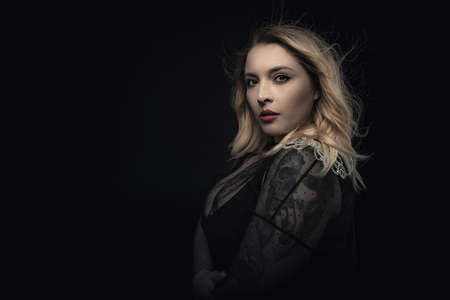 Fashion portrait of young woman blonde in transparent evening dress. Blowing hair, professional makeup with red lips. Beauty of elegant plus size model. Stylish shot with copy space. Black background.の写真素材