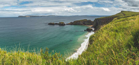 Coastal Scenery Nothern Ireland Nature Landscape. Seaside Tourism Place Rocky Island Beach. Amazing View on Shoreline from Climb on Ocean Green Water and Waves. Shiny Day and Cloudy Skyの写真素材