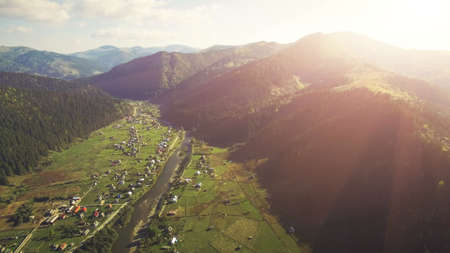 Aerial Drone Footage View: Flight over sunny village with houses, forests, fields and river in sunrise soft light. Carpathian Mountains, Ukraine, Europe. Majestic nature landscape. Beauty world.の写真素材