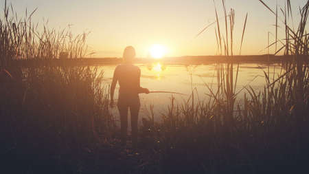 Aerial Drone View: Flight over the woman fishing on the river coast. Sunset soft light. Magestic landscape. Sport recreation background.の写真素材