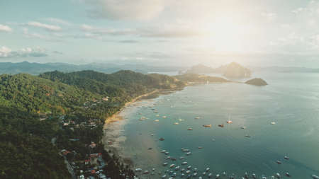 Ocean pier town aerial: sun cityscape with lot of boats, ships, vessels at waterfront. Cottages and lodges at green palm trees on hills. Water transport at tropic Filipino resort of Palawan islandの写真素材