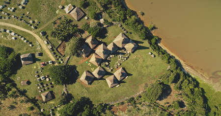 Top down traditional village at green grass valley on sea coast aerial view. Indonesia landscape of tropical nature at sand ocean bay. Unique buildings at countryside road in birds-eye drone shotの写真素材