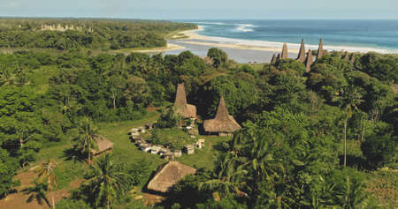Picturesque village with traditional houses on sand coast of sea bay in aerial view. Green tropic nature landscape at ornately roofs. Unusual buildings landmark in primitive settlement of Indonesiaの写真素材