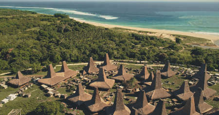 Seaside long-held tradition village with unique ornately roofs houses aerial view. Indonesia landmark at green ocean coast with sand beach. Greenery countryside landscape of Sumba Island, Asiaの写真素材