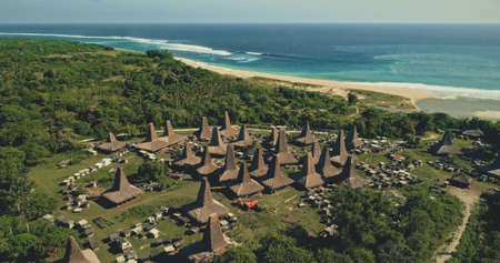 Amazing seaside traditional village with unique designed roofs houses aerial view. Indonesia tourist attraction at green valley with tropic trees near ocean bay. Cinematic scenic landscape drone shotの写真素材