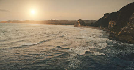 Sun set seascape of sea bay cliff coast aerial view. Nobody nature scape of tropic island with sand beach. Wonderful summer scenery of Indonesia holiday tour at Sumba isle. Cinematic sunset drone shotの写真素材