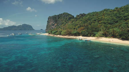 Ocean bay harbour with boats and passengers at sand beach aerial view. Panoramic landscape of tropic island with tourist. Green forest at shore with travelers at vessels on Palawan Isle, Philippinesの写真素材